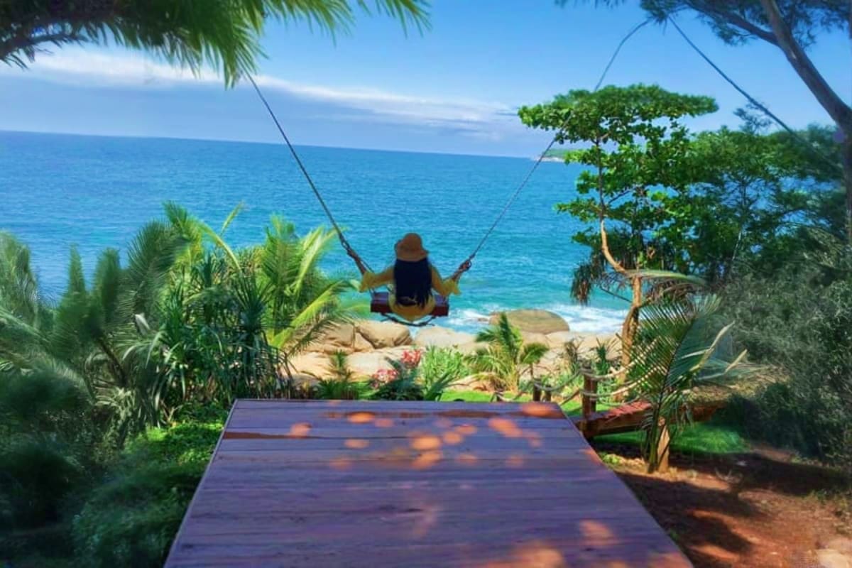 Rock Beach Swing Person on rope swing suspended over rocky beach with turquoise ocean and tropical vegetation