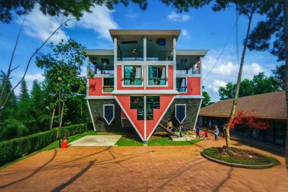 The Upside Down House Museum Upside Down House Museum with inverted architecture, red and white facade, surrounded by trees and visitors on the grounds