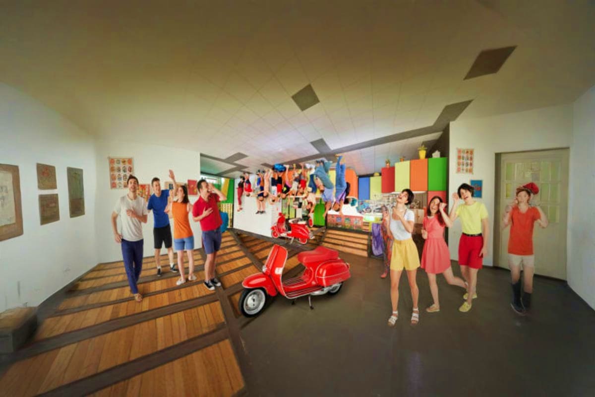 The Upside Down House Museum Interior view of The Upside Down House Museum with visitors standing among inverted furniture and a red Vespa scooter suspend