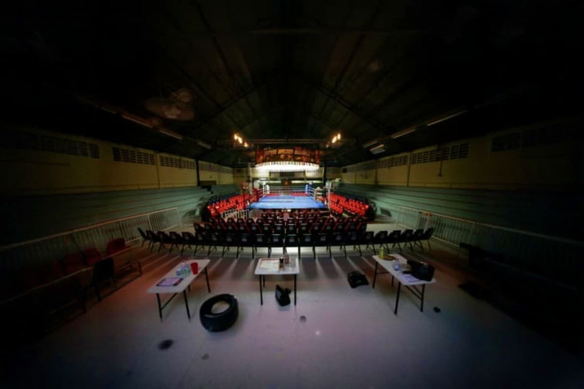 Patong Boxing Stadium Interior view of Patong Boxing Stadium with blue boxing ring, red-robed fighters seated ringside, and arena seating under ind