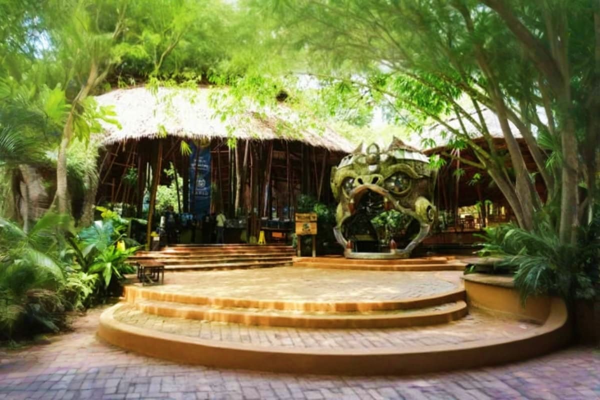 Tropical thatched-roof building with stone monkey statue in lush garden courtyard surrounded by tall trees at Hanuman World a