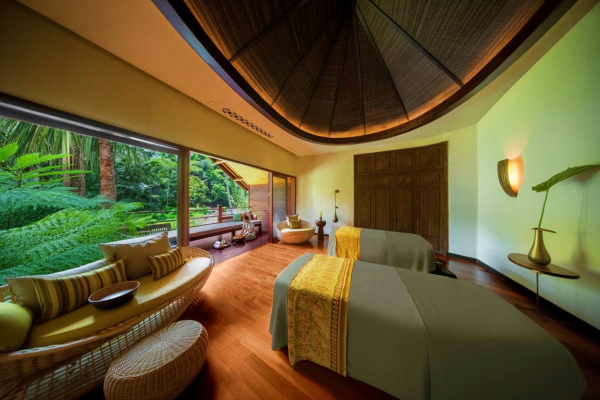 Luxurious spa treatment room with wooden dome ceiling, twin massage beds, woven rattan seating, and tropical garden views thr