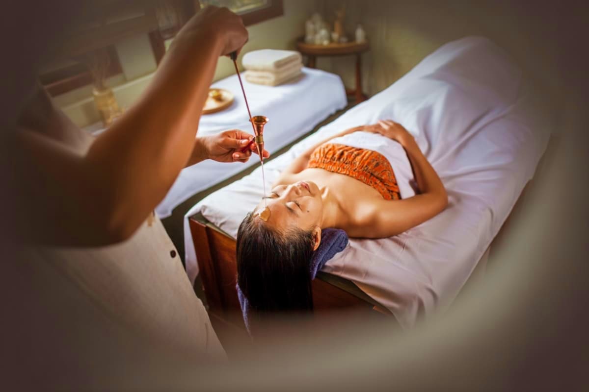 Therapist performing traditional Balinese spa treatment with oil drip on client's forehead at Frangipani Esthetics in Nusa Du