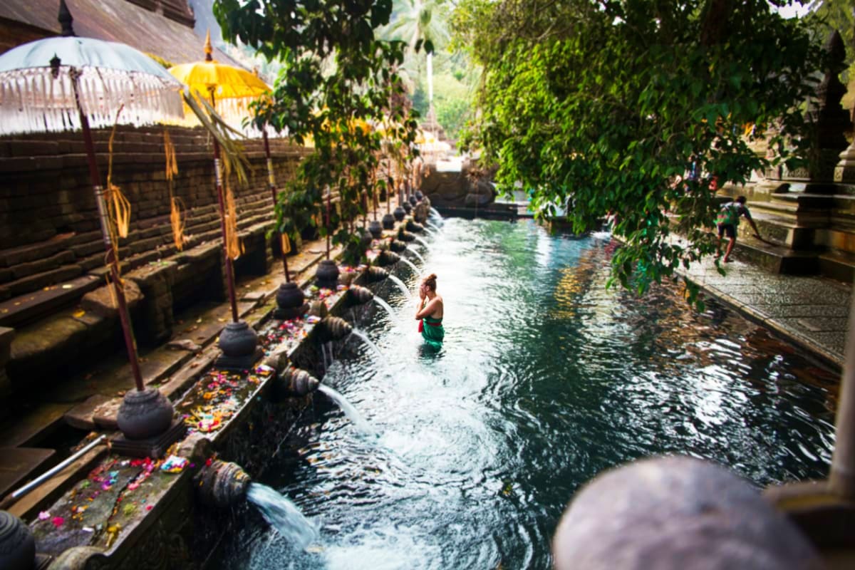Tourist performing purification ritual bathing in sacred spring water channel at Tirta Empul Temple in Bali with yellow umbre