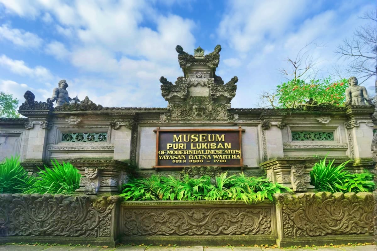 Museum Puri Lukisan entrance gate with ornate stone carvings, decorative guardian statues, and lush tropical plants in Ubud, 