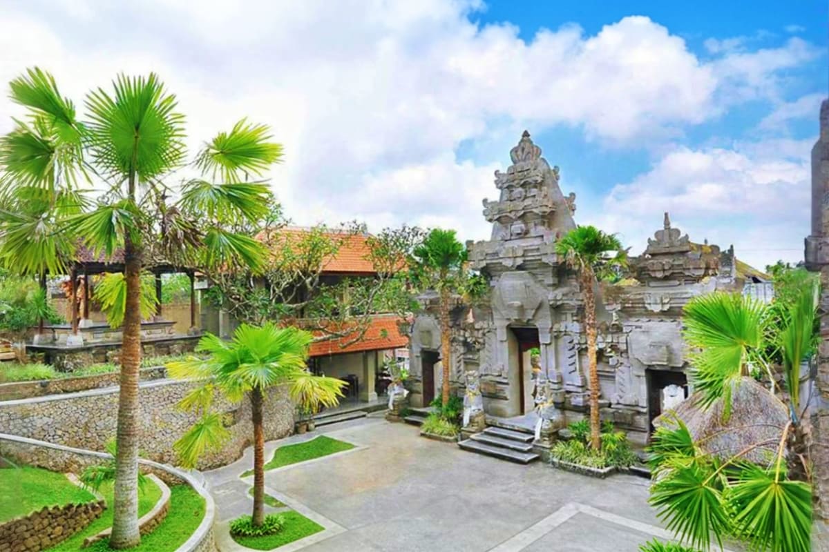 Traditional Balinese temple courtyard at Museum Puri Lukisan with ornate stone structures, palm trees, and manicured gardens 