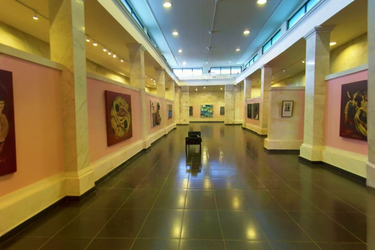 Modern art gallery interior with pink walls, white columns, polished dark floor, and framed artworks displayed along both sid