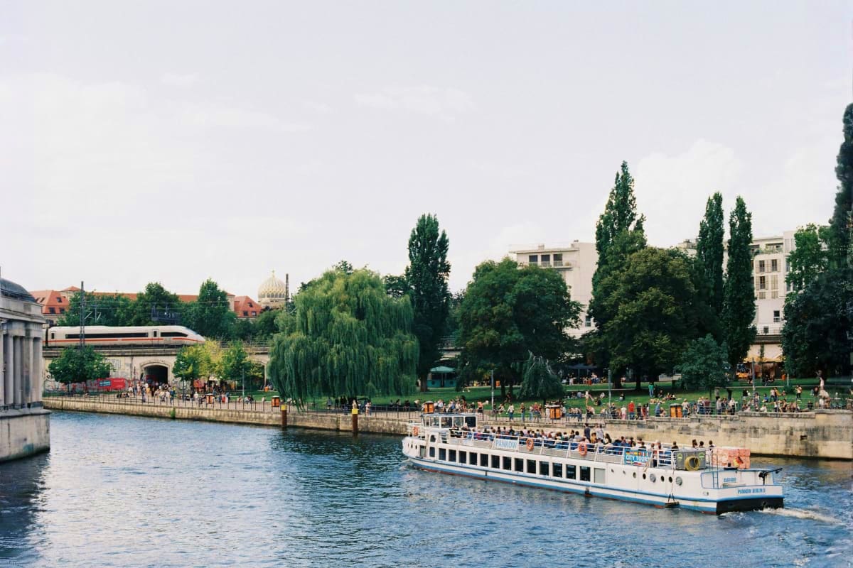 Tourist riverboat cruise on the Spree River in Berlin with city buildings, trees, and park along the waterfront