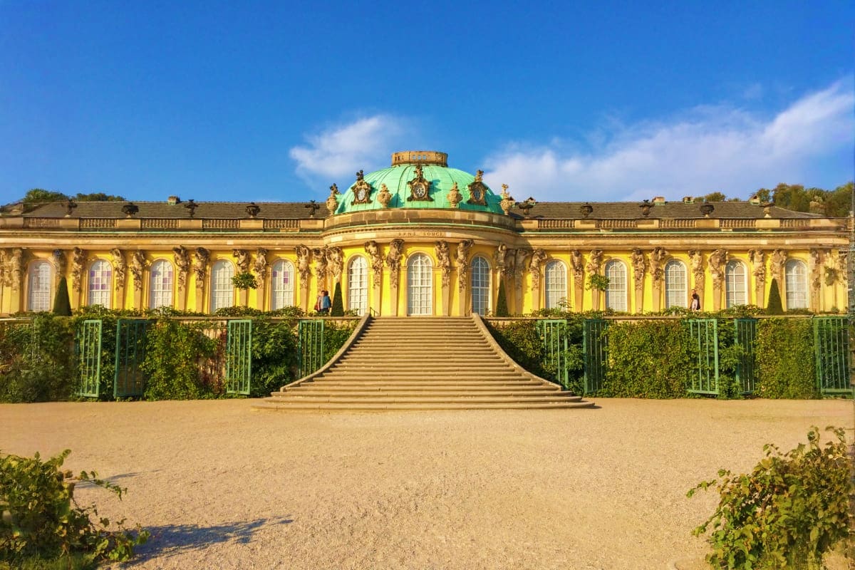 Sanssouci Palace facade with yellow walls, green dome, grand staircase, and manicured gardens in Potsdam