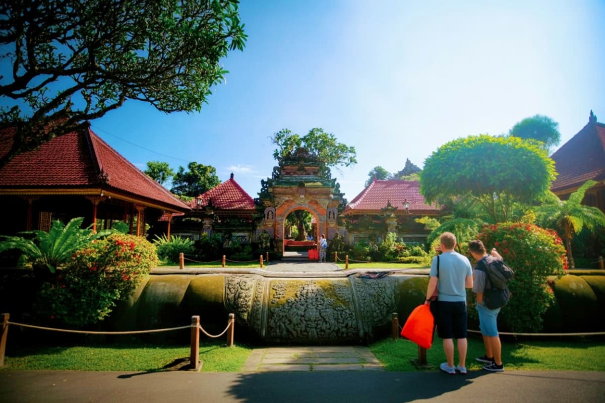 Tourists viewing ornate stone barrier with carved details at Ubud Palace entrance, traditional Balinese temple architecture w
