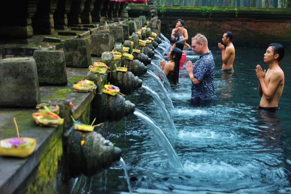 Tourists bathing in sacred spring water pools at Tirta Empul temple with stone spouts and flower offerings in Bali