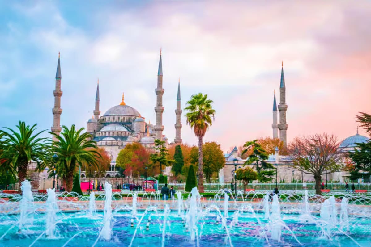 Blue Mosque with multiple minarets and golden dome viewed from fountain plaza in Istanbul at sunset with palm trees and autum