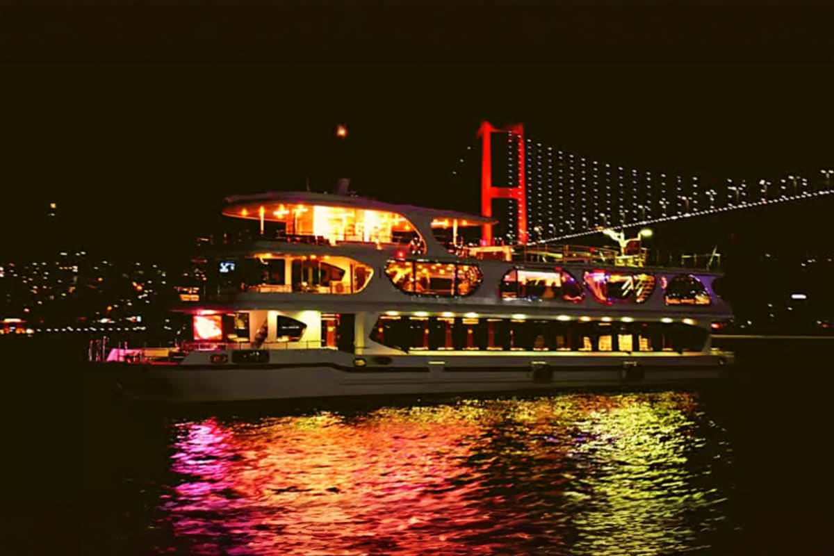 Illuminated ferry boat on the Bosphorus at night with the lit 15 July Martyrs Bridge visible in the background