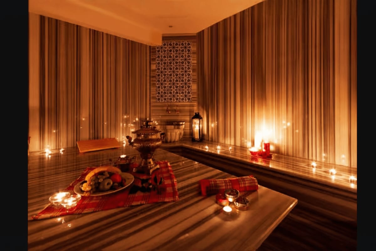 Luxurious Turkish hamam spa interior with warm lighting, red cushions, traditional brass vessels, and decorative candles on w