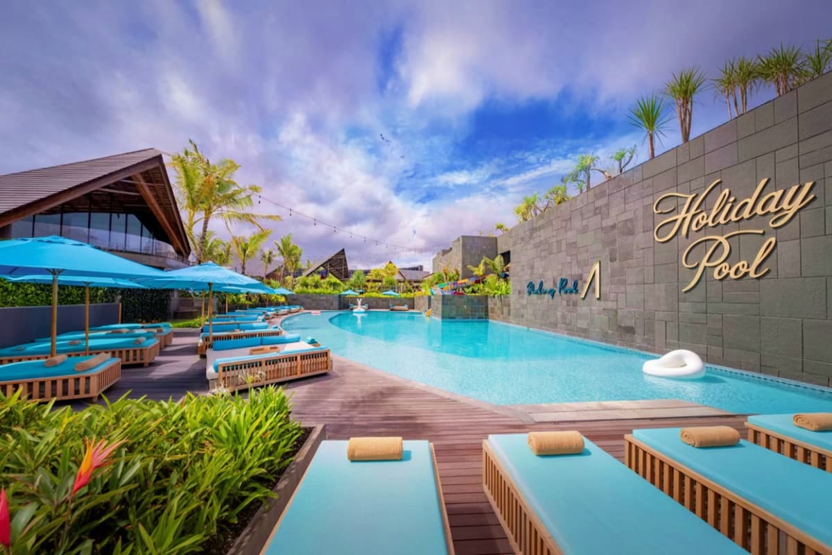 Atlas Beach Club holiday pool with turquoise water, wooden loungers, blue umbrellas, palm trees, and modern architecture