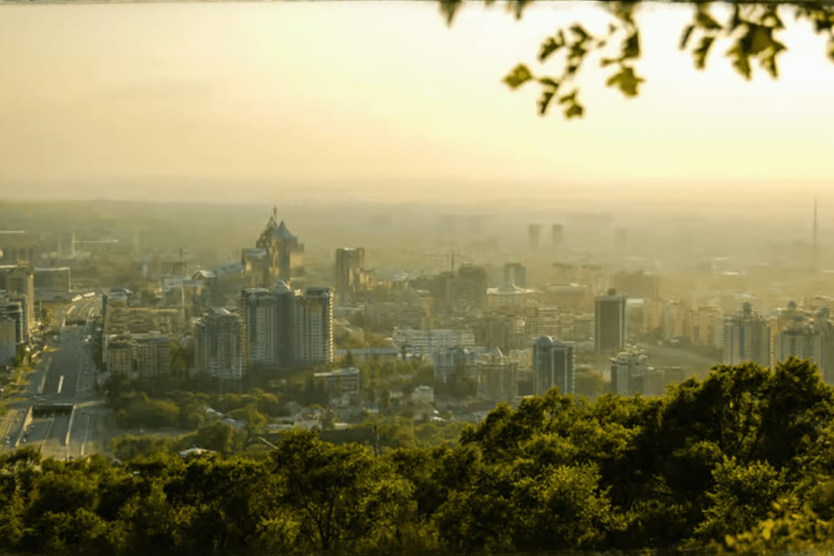 Panoramic cityscape view of Almaty skyline with golden-domed cathedral, residential buildings, and tree-covered hillside in f