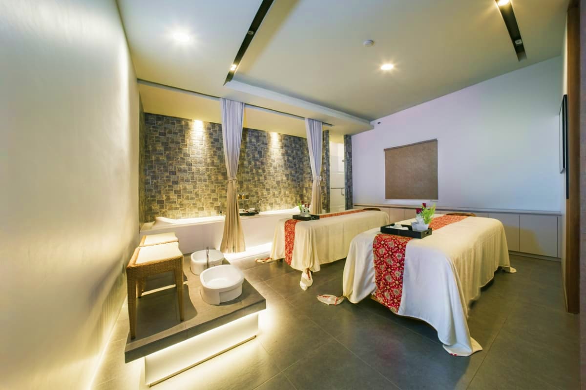 Modern spa treatment room with two massage beds, soaking tub with mosaic tile surround, and ambient lighting at Jasmine Aroma