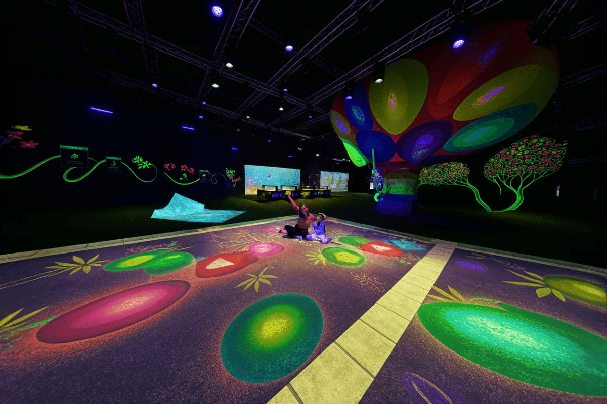 Interactive digital art installation at PlayLab with glowing floor projections, colorful suspended inflatables, and visitors 