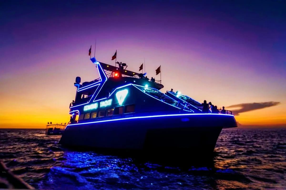 Illuminated cruise boat with blue neon lights on ocean water during sunset with purple and orange sky