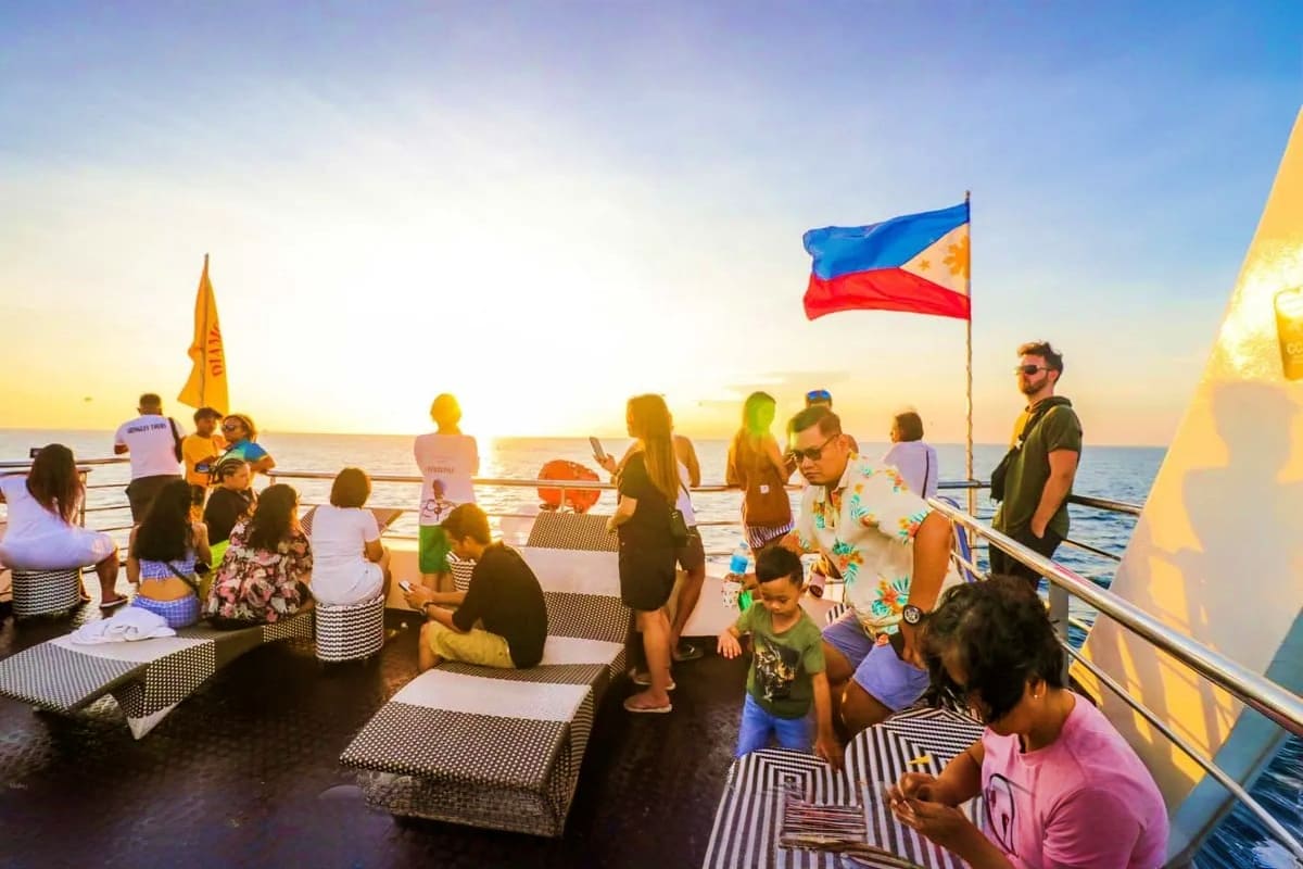 Passengers enjoying sunset aboard a cruise ship with Philippine flag flying, ocean and golden sky in background