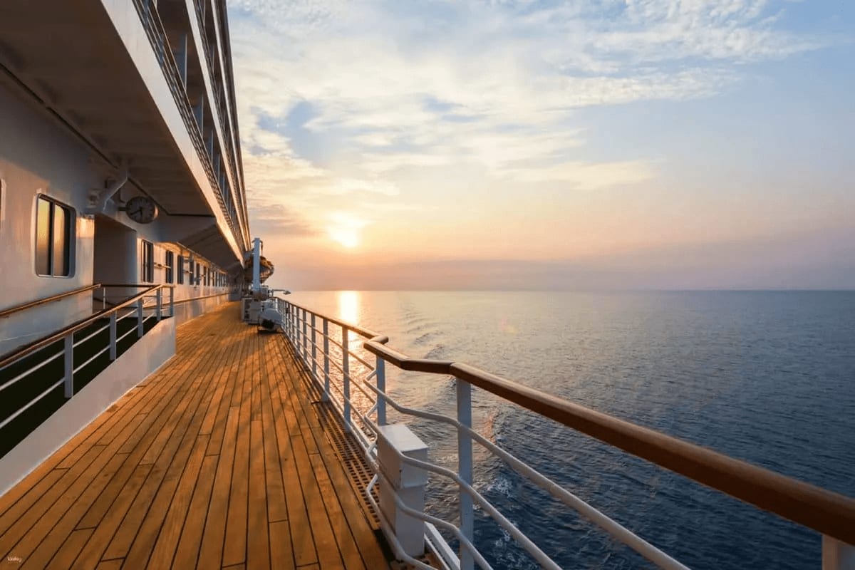 Cruise ship deck at sunset with wooden promenade, metal railing, and calm ocean horizon during golden hour