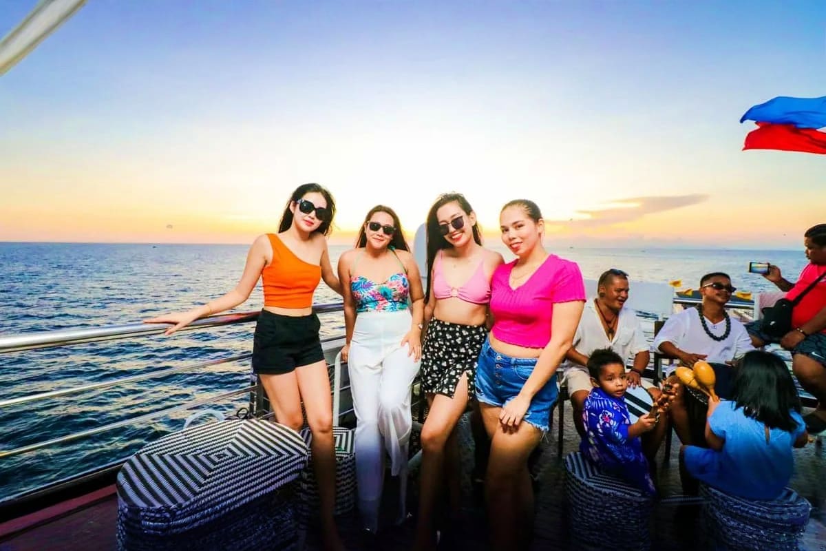 Four women wearing sunglasses on a boat during sunset over the ocean with other passengers aboard