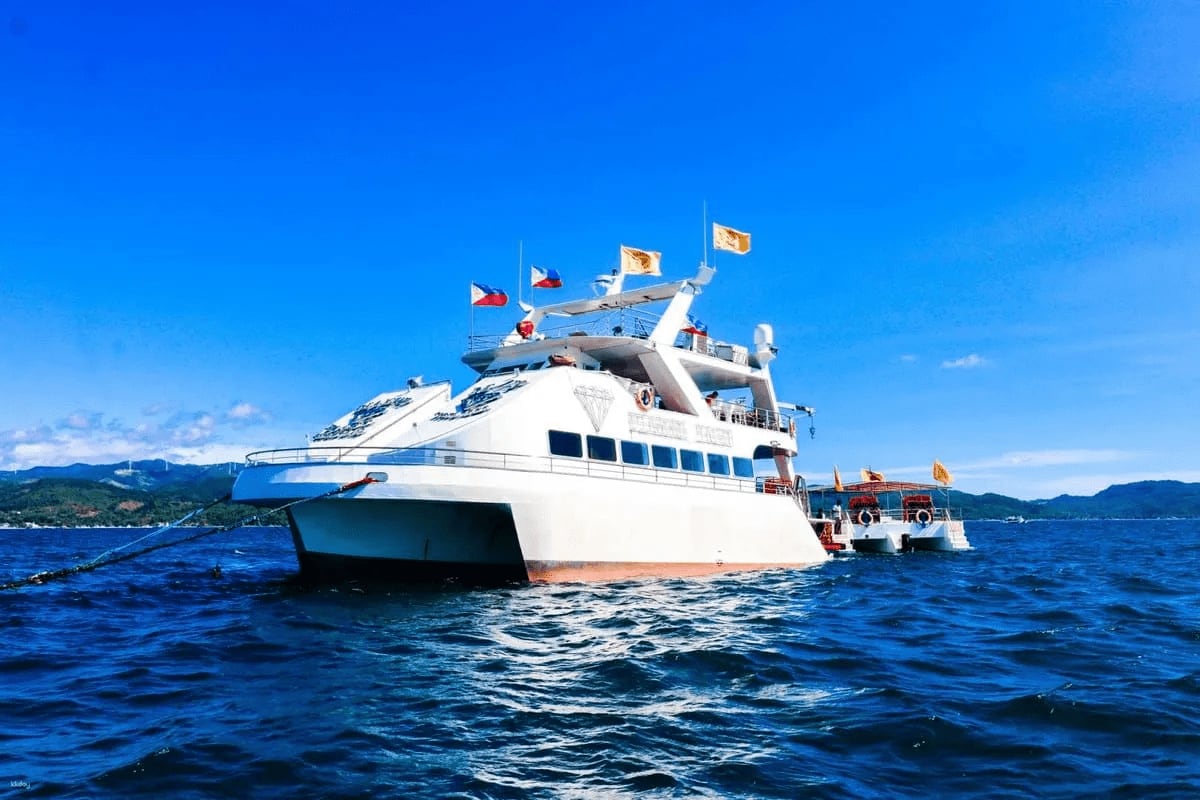Luxury white and blue yacht anchored in deep blue ocean waters with Philippine flags, mountains visible in background
