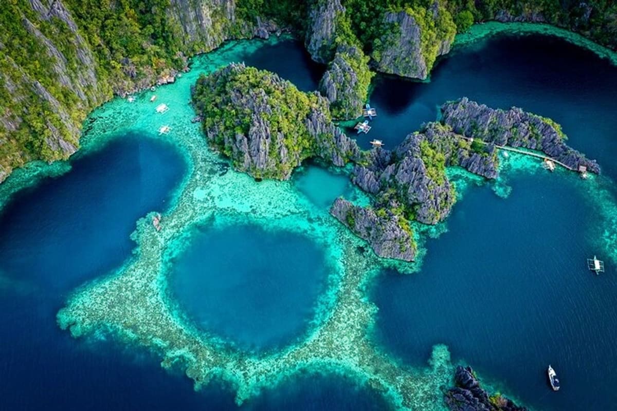 Aerial view of Coron Island's turquoise lagoons surrounded by limestone cliffs, tropical vegetation, and tour boats on crysta