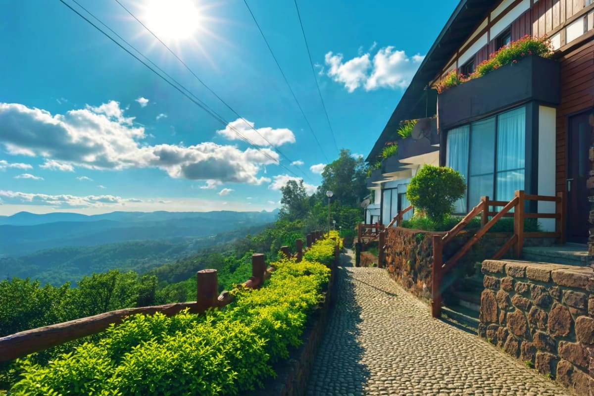 Modern mountain resort building with stone facade and wooden railings overlooking forested hills under blue sky
