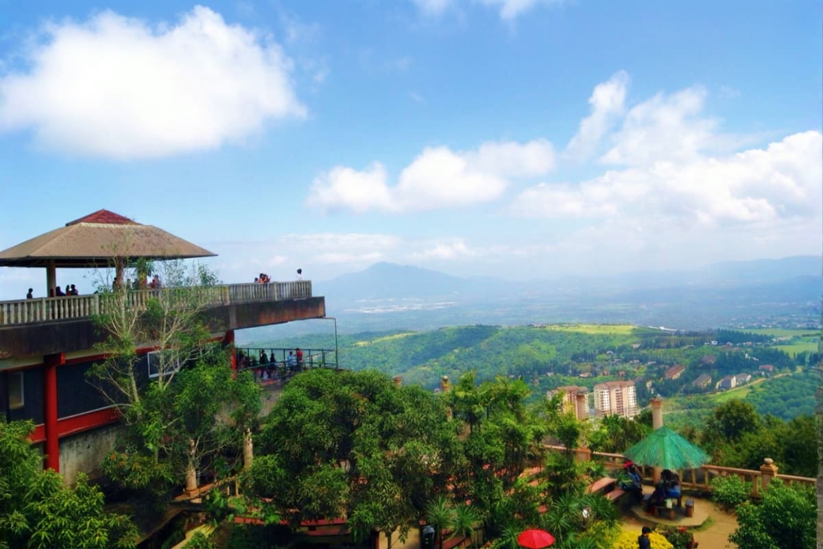 Elevated viewpoint of Tagaytay ridge with thatched-roof observation deck overlooking valley, mountains, and distant settlemen