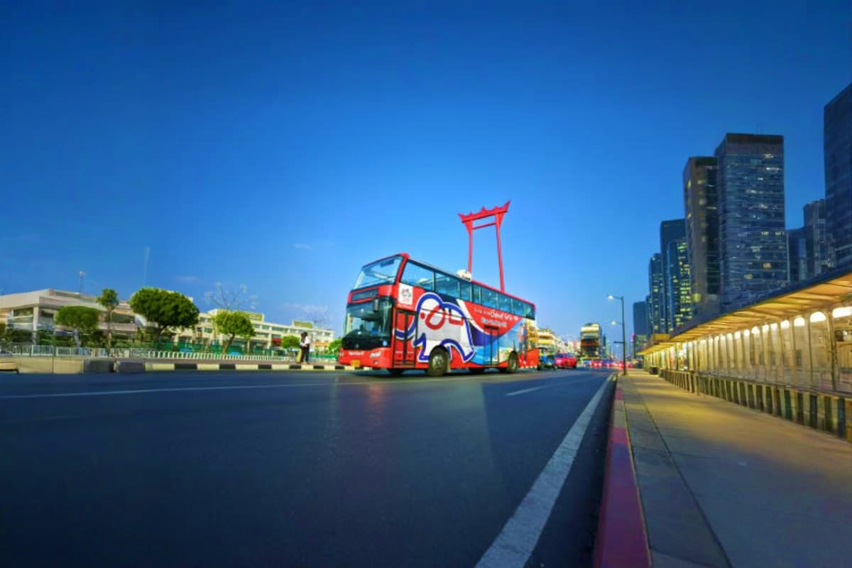 Red double-decker hop-on-hop-off tour bus with traditional Thai architectural roof element in Bangkok city street with modern