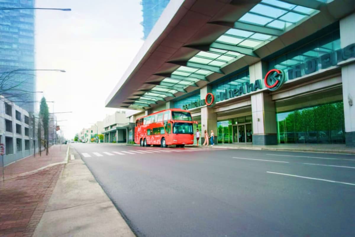 Red double-decker hop on hop off tour bus stopped at modern shopping mall with glass canopy in Bangkok city street