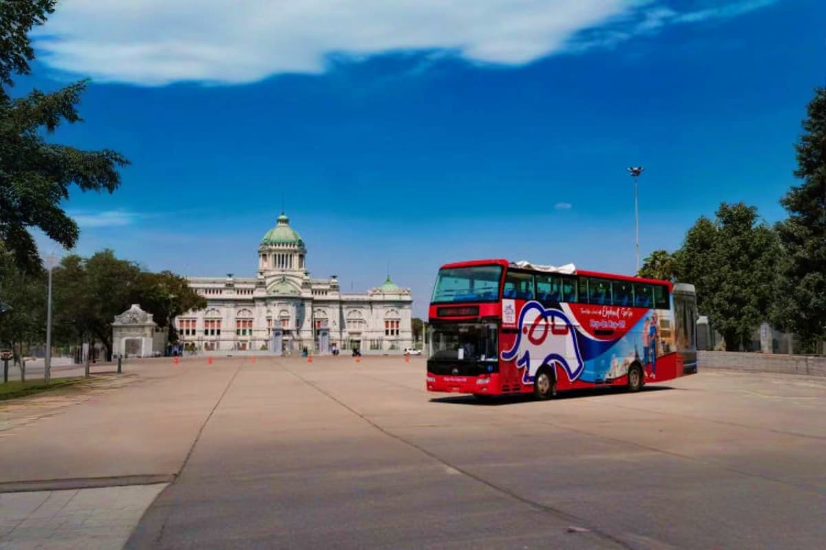 Red double-decker tour bus parked in front of the Grand Palace in Bangkok with clear blue sky