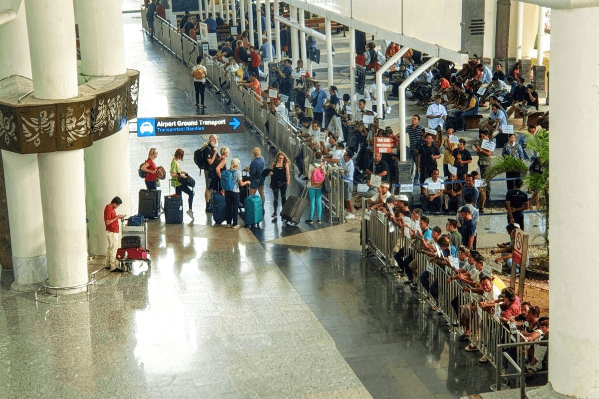 Crowded airport terminal with passengers waiting in queue lines near Airport Ground Transport sign at Bali airport