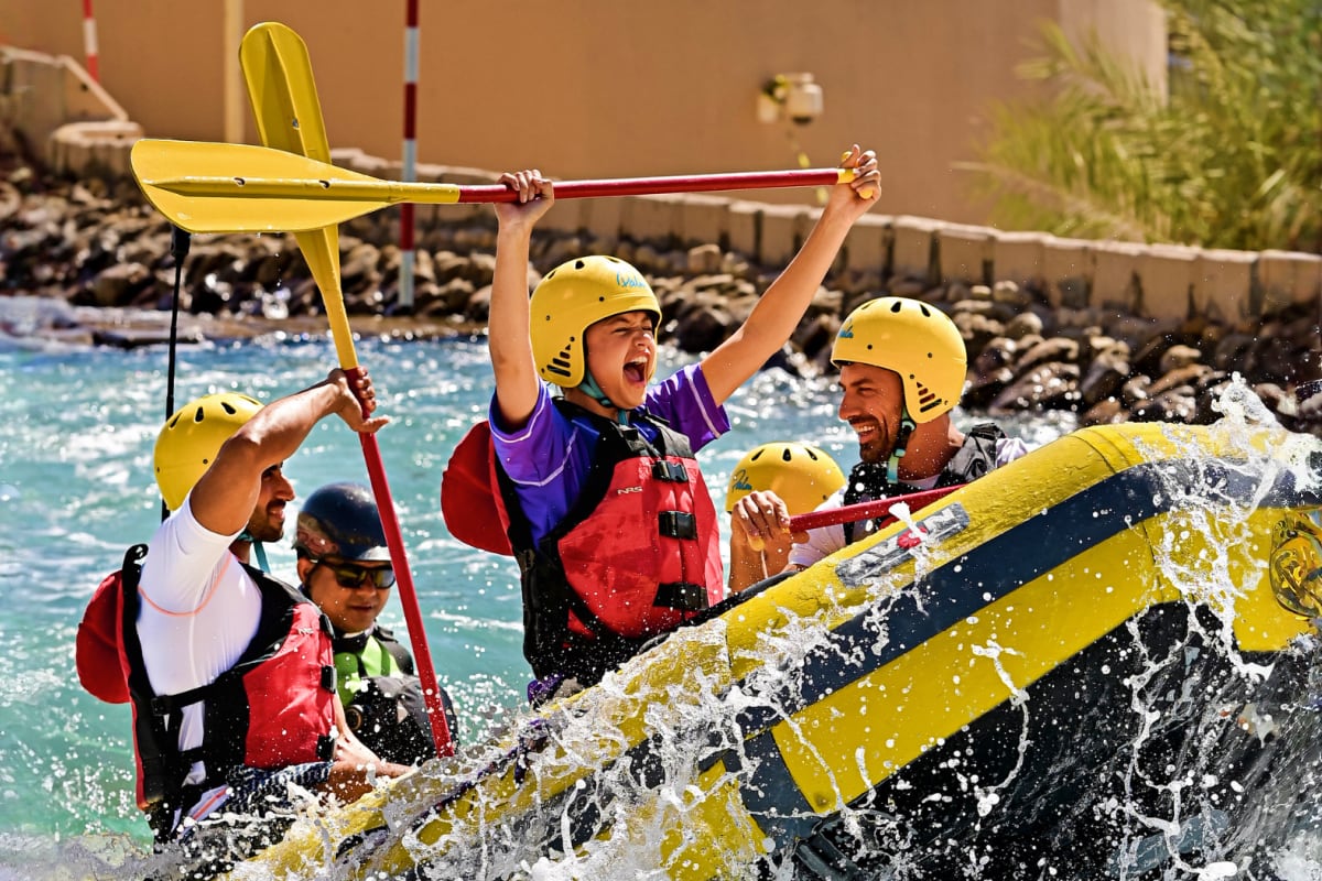 Group of people white water rafting in yellow raft wearing yellow helmets and red life jackets on turquoise river with rocky 