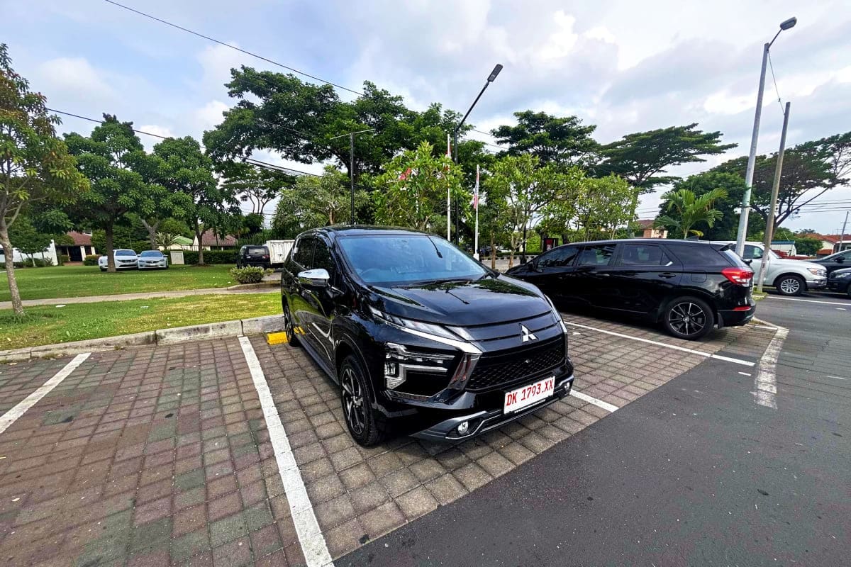 Black Mitsubishi Xpander parked in a paved lot with trees and street lamps visible in background