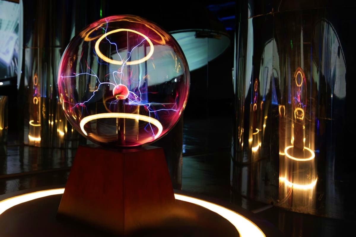 Plasma ball with red, purple and yellow electric tendrils inside glass sphere on red pedestal in dark exhibition space with n