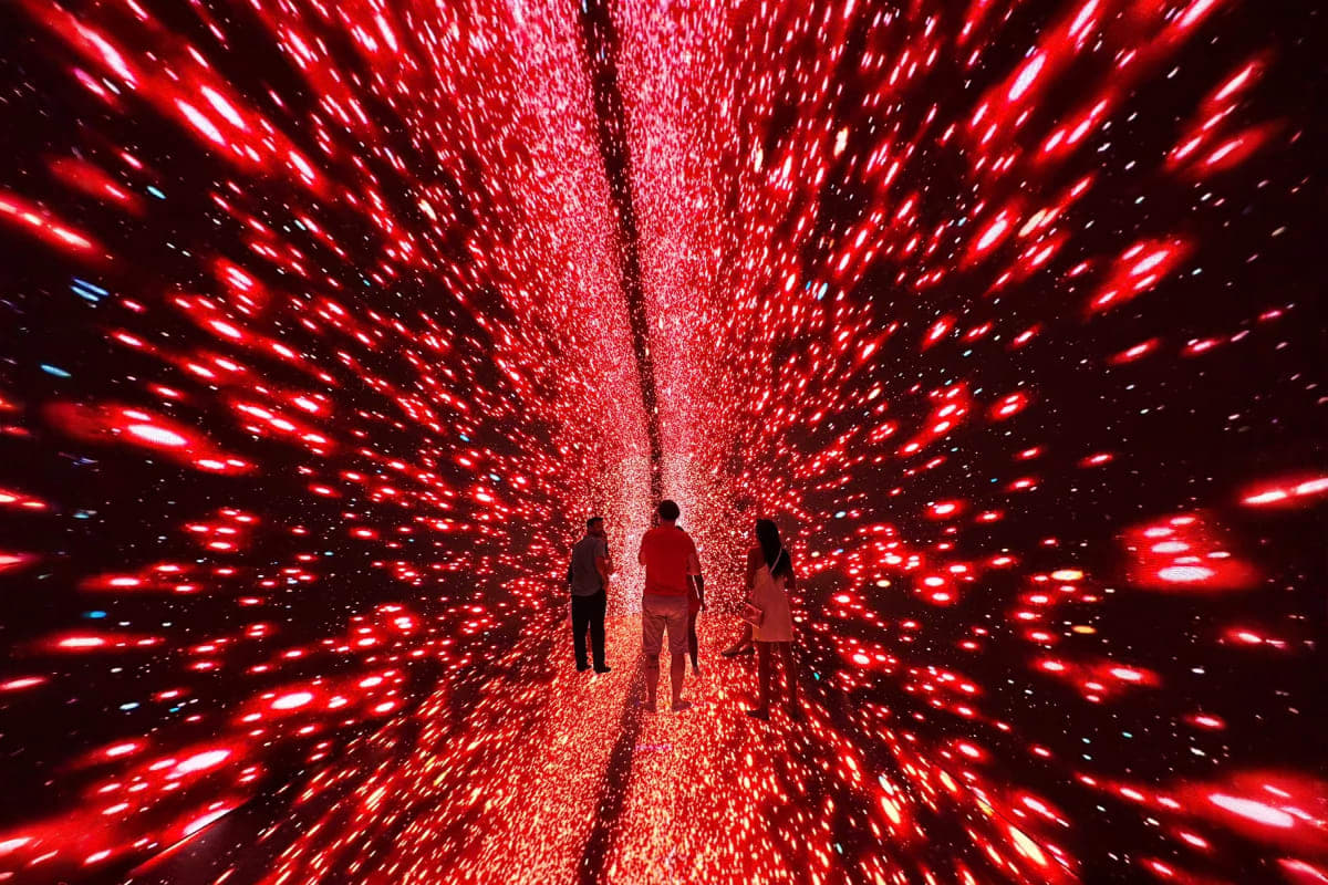 Three visitors standing in immersive red light installation with glowing particles creating tunnel effect