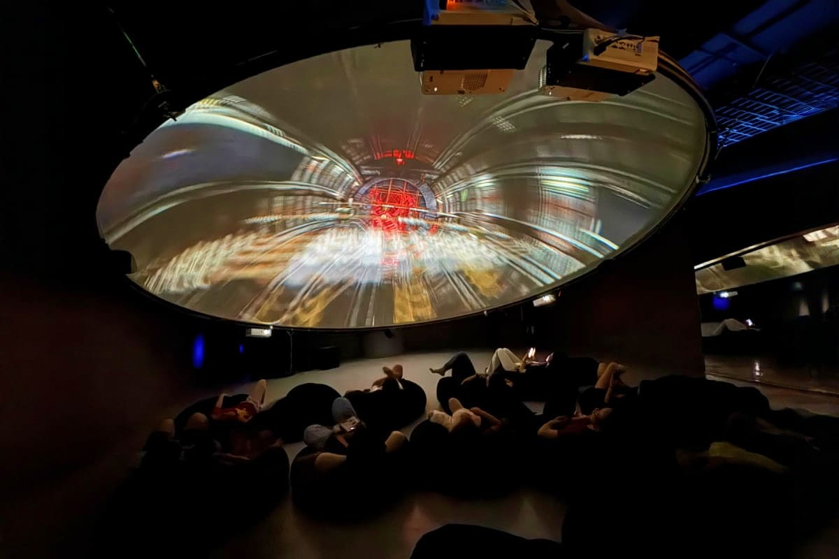 Audience watching immersive digital art projection on large dome screen with red center light design in darkened theater spac
