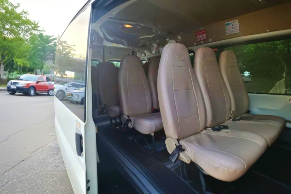 Interior view of white passenger van with beige seats and open sliding door at airport pickup location