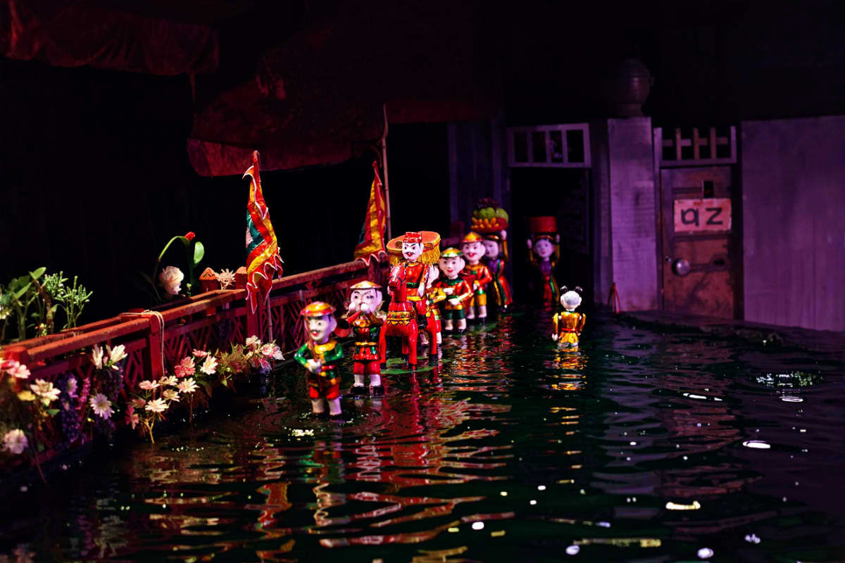 Traditional Vietnamese water puppet show with ornate puppets in red costumes performing on water stage with decorative flower