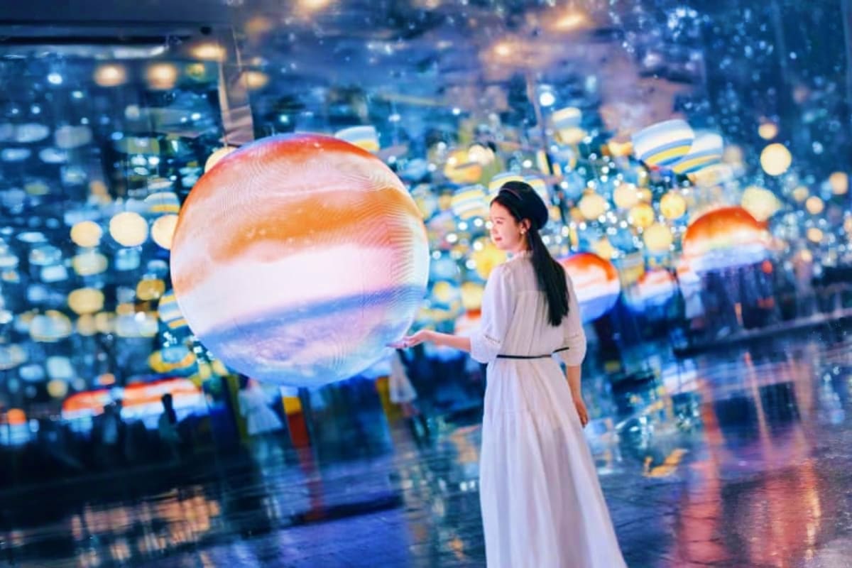 Woman in white dress standing before illuminated spheres with Netherlands flag colors against blurred city lights backdrop