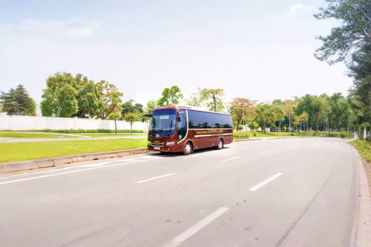 Danang Airport Drop off Maroon tour bus driving on a wide road lined with green trees and grass fields in Danang