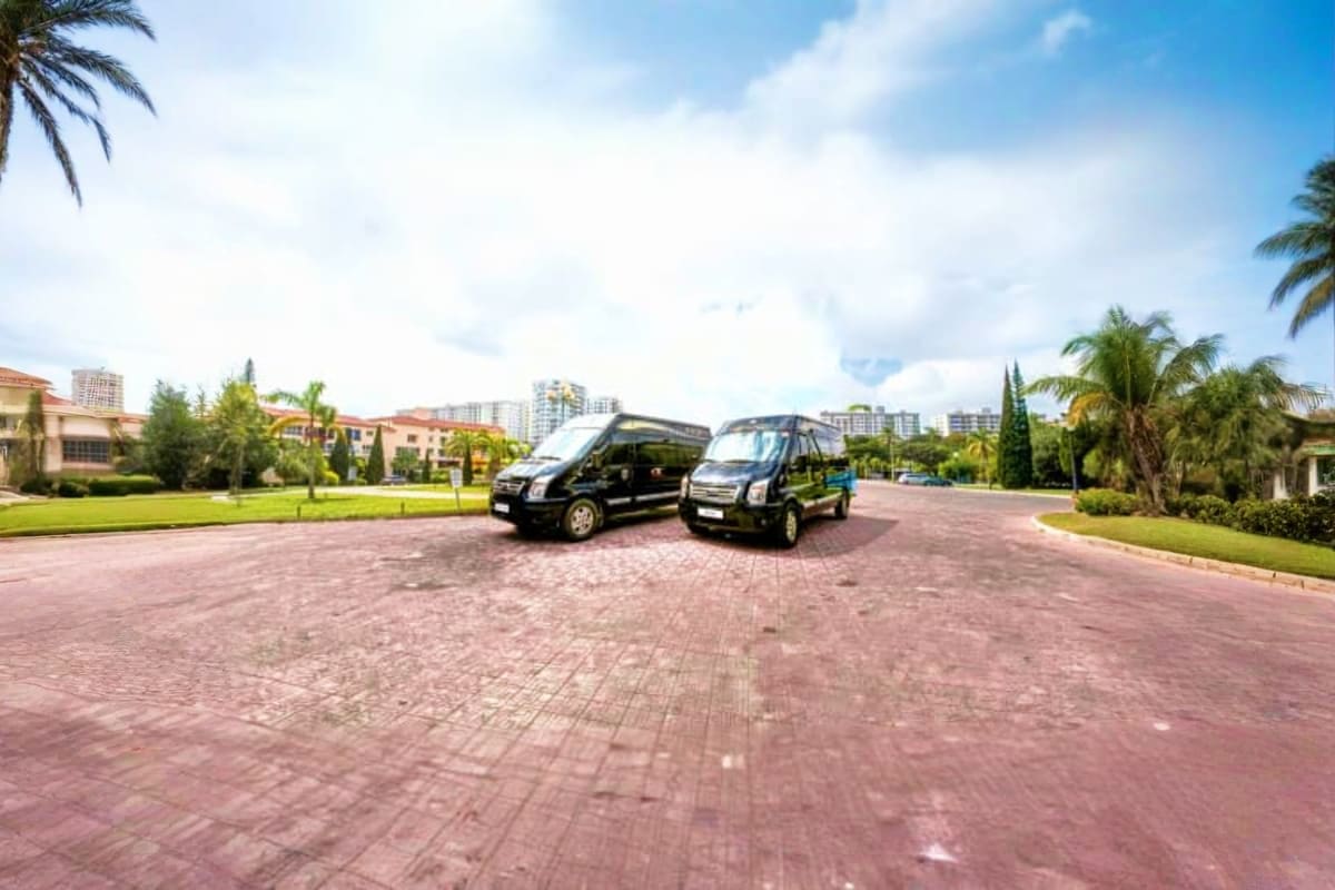 Two black shuttle vans parked on brick driveway at luxury resort with palm trees and city skyline in background