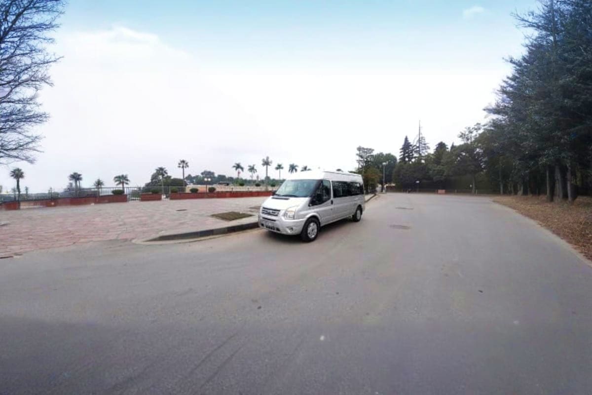 White minivan parked in empty plaza with palm trees and red brick wall in background, Danang airport transfer vehicle