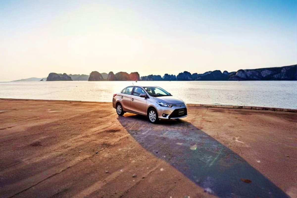 Silver sedan parked on sandy beach with limestone karst mountains and calm bay water in background at Danang coastal location