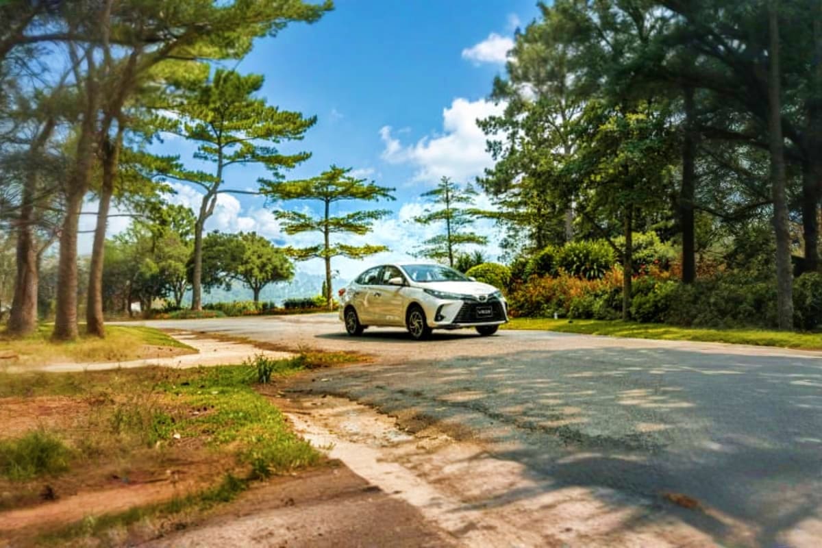White Toyota car parked on tree-lined road in Da Nang with blue sky and mountains in background