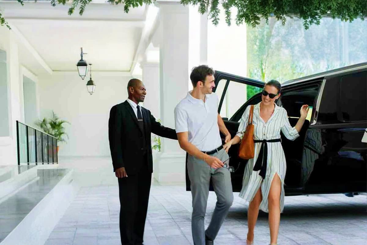 AAU Delegates Umrah Sharing Transfer Concierge service at luxury hotel entrance with man and woman exiting black SUV while bellhop assists with luggage under cove