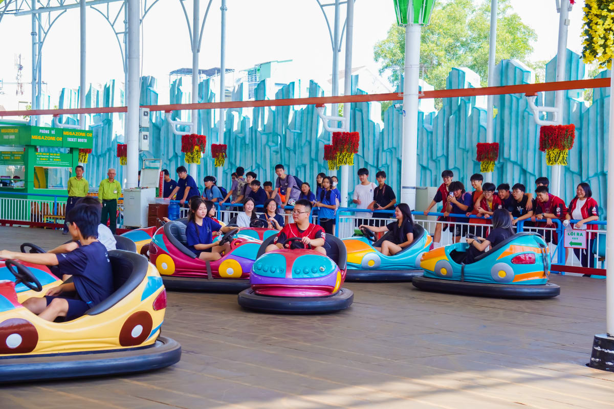 Colorful bumper cars ride at Suoi Tien Theme Park with multiple vehicles and riders on track, spectators standing behind barr