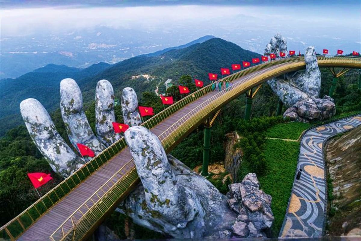 Golden Bridge with giant stone hands and Vietnamese flags in Da Nang mountains with forested valley below
